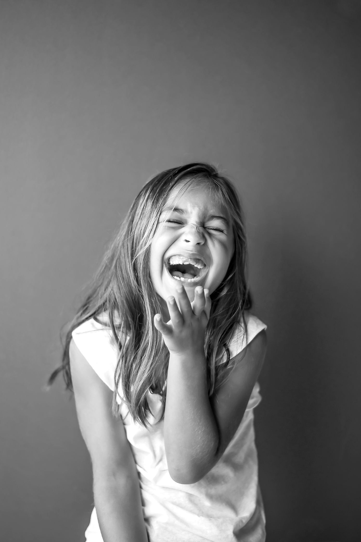Black and white portrait of child laughing with hand near face.