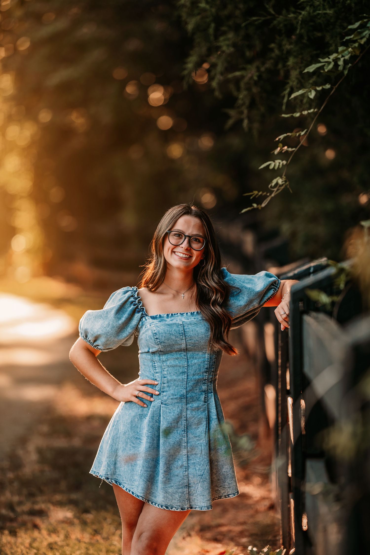 Woman in denim dress poses outdoors during golden hour sunset.