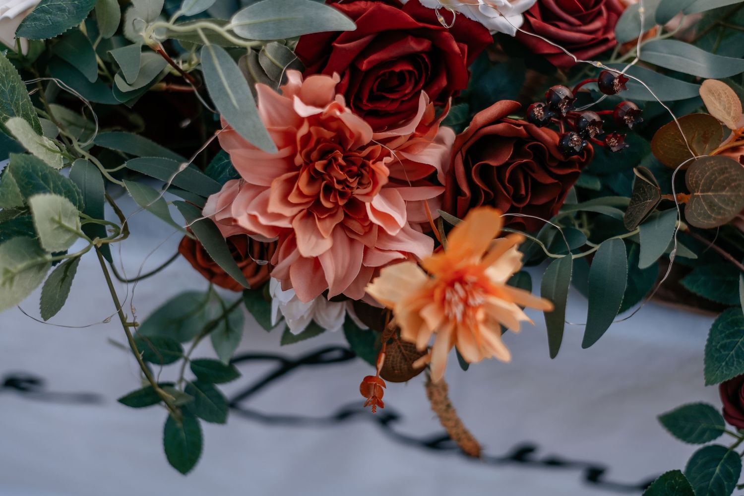Lush autumn wedding bouquet featuring deep red roses, blush dahlias, and eucalyptus greenery with rich burgundy accents.