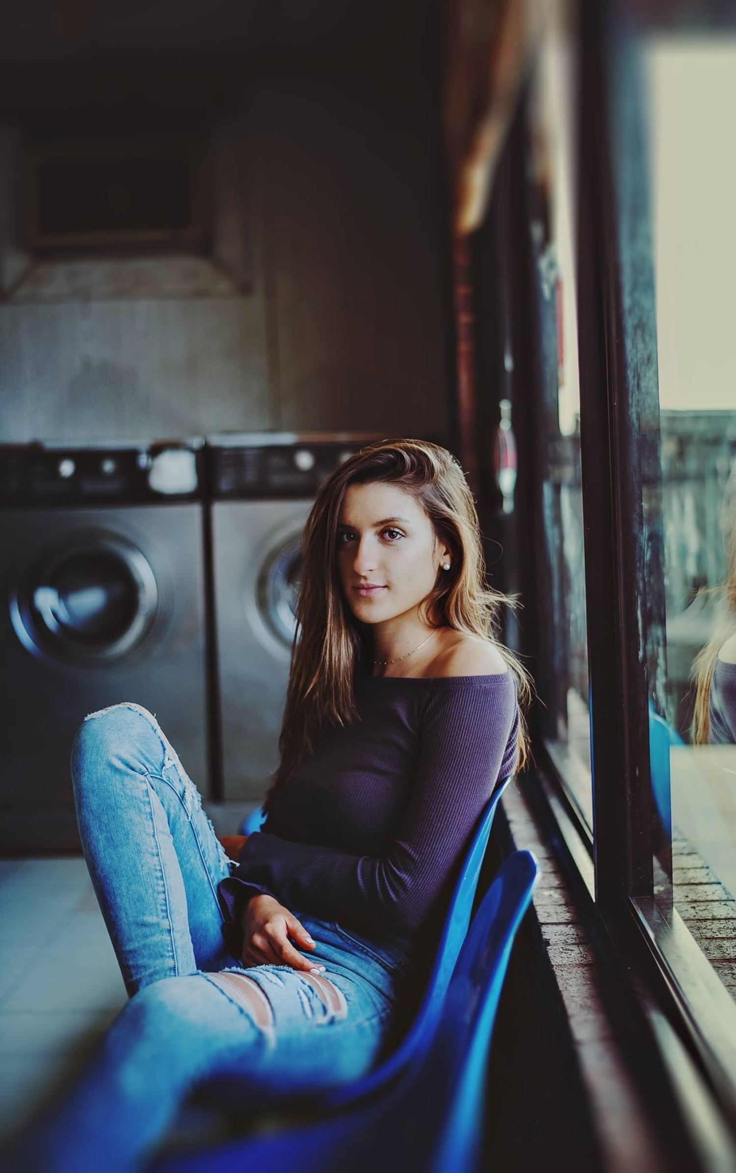 A person in a navy top and jeans lounges on a blue chair in moody indoor lighting.
