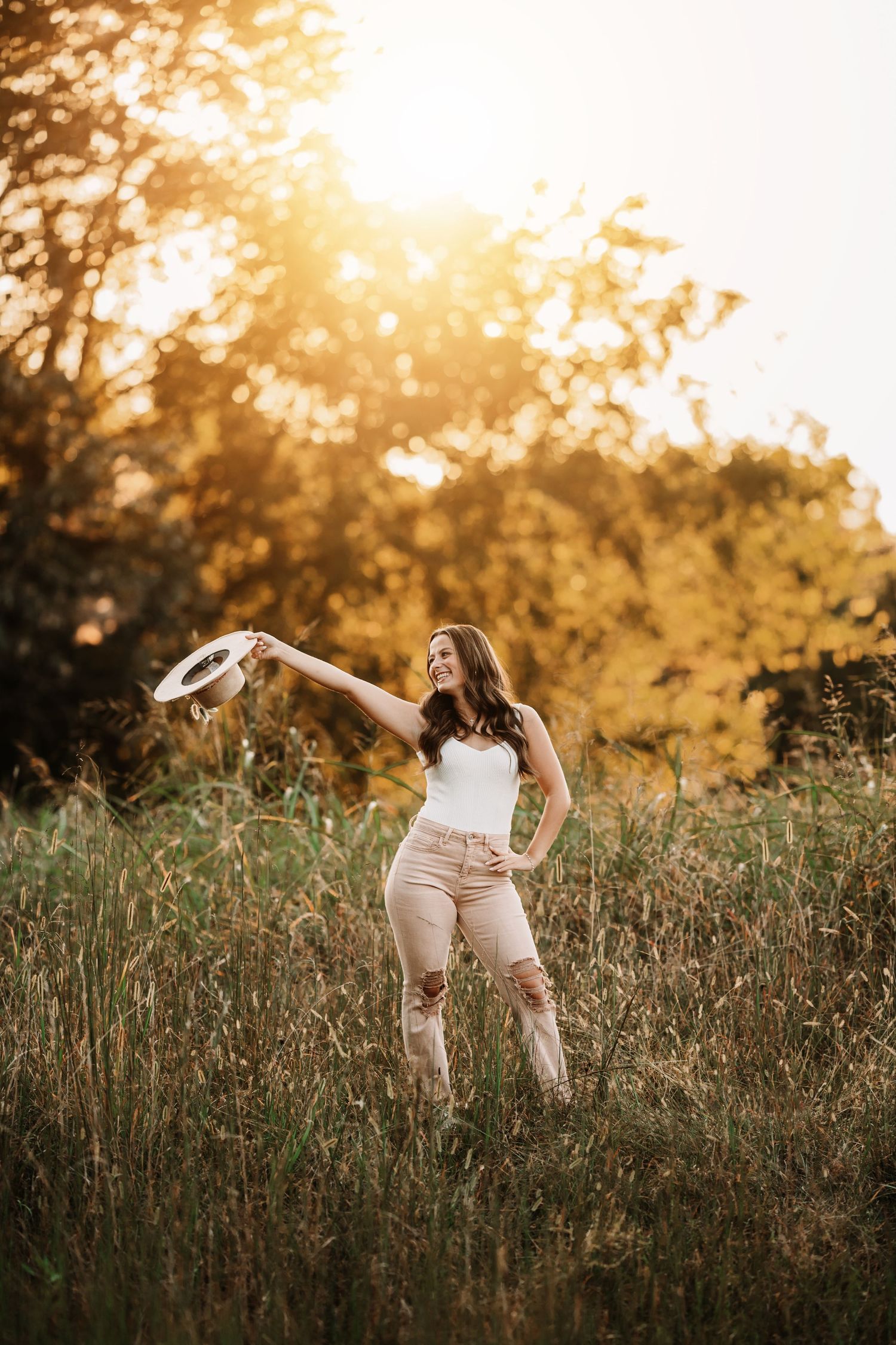 Woman in white top and beige pants dancing in sunlit meadow.