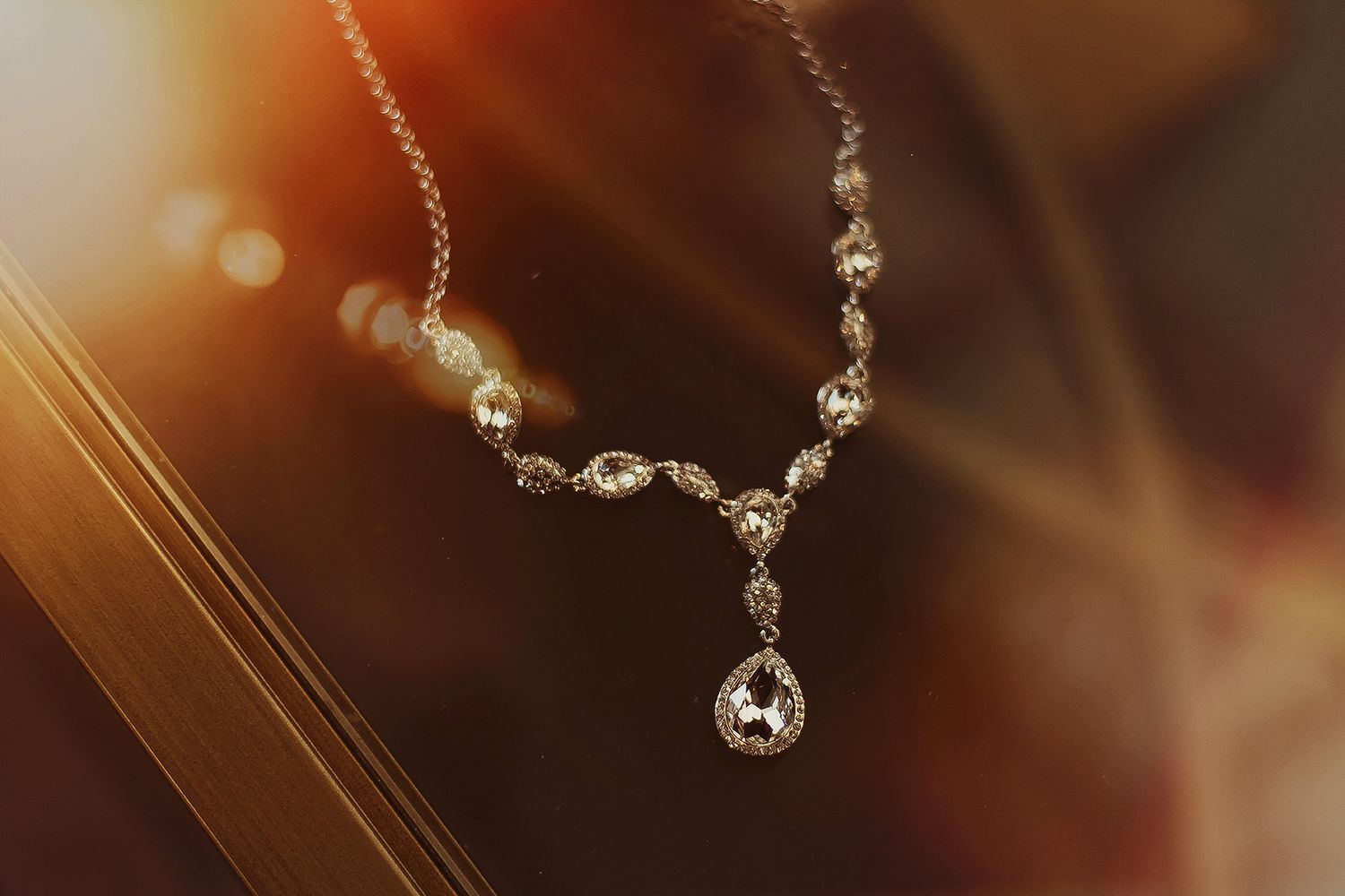 Elegant diamond drop necklace with teardrop pendant on delicate chain, photographed in warm golden bokeh light.