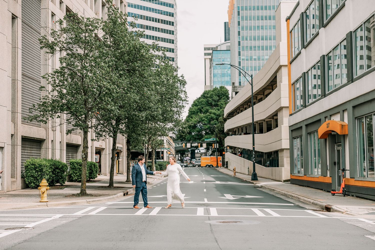 Couple holding hands crossing a zebra crossing in an urban city street surrounded by tall buildings.