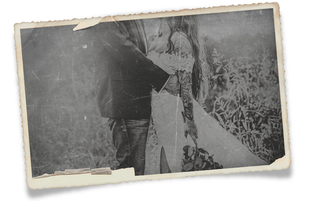 Vintage black and white photograph of a couple embracing outdoors, aged and worn with torn edges.