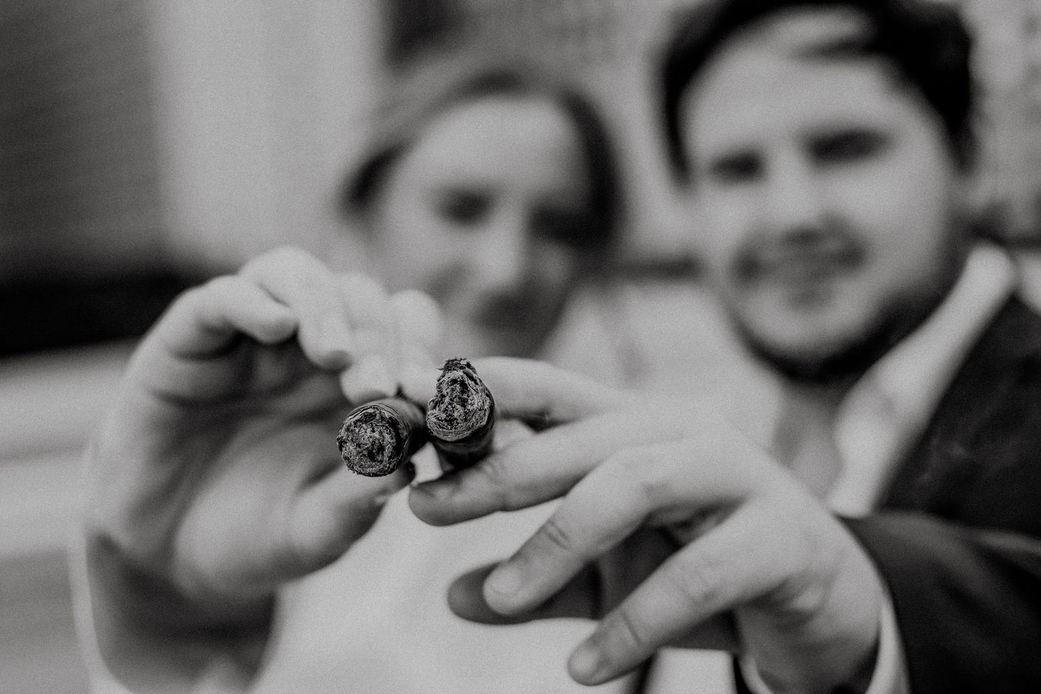 Black and white photo of a couple holding up two ornate wedding rings toward the camera at their wedding ceremony.