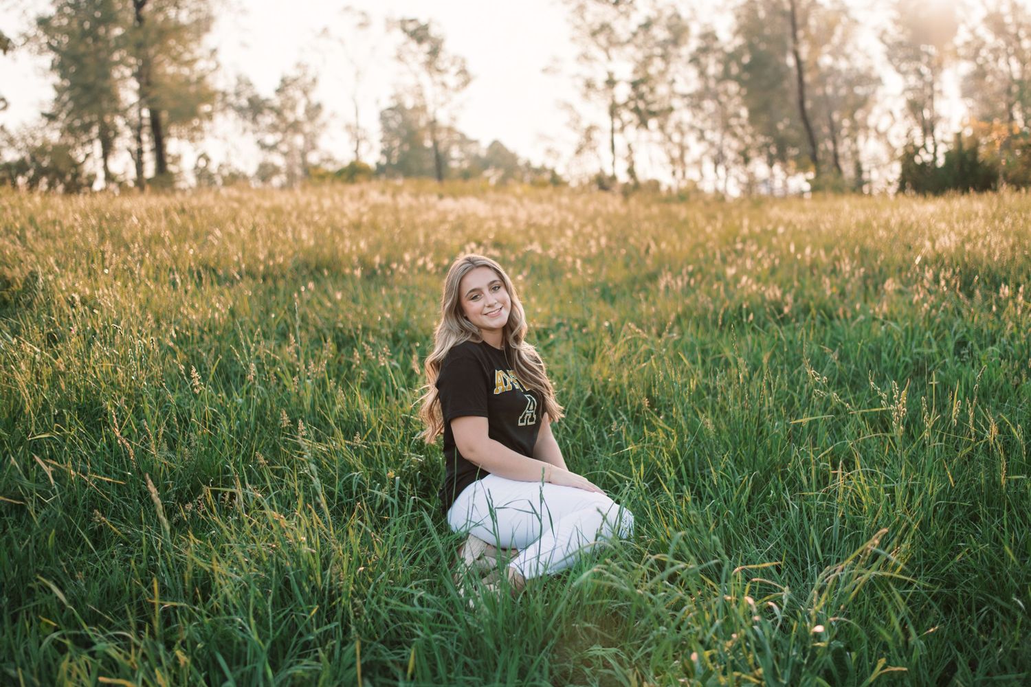 Person sitting in tall grass field during golden hour.