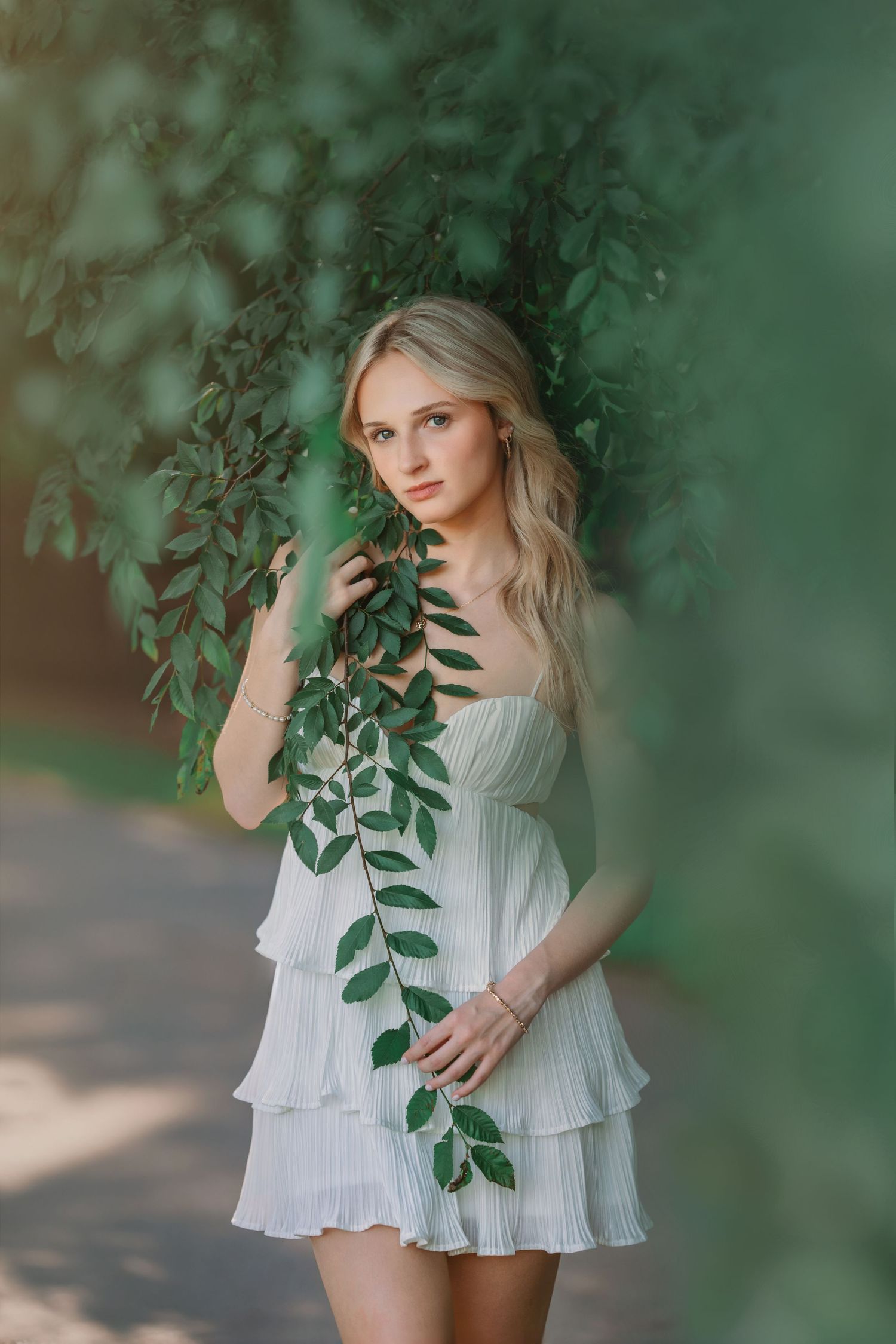 Woman in white dress posing elegantly with hanging green foliage in soft natural lighting.