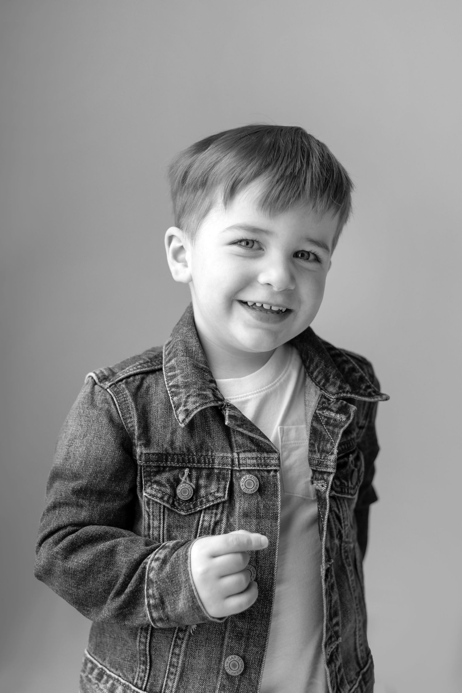 Black and white portrait showing joyful expression while wearing casual denim jacket.