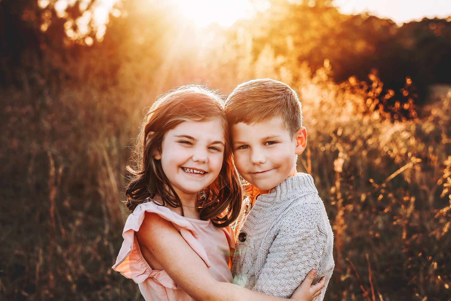 Two happy children hugging in a golden sunlit field, smiling warmly in a heartwarming outdoor portrait.