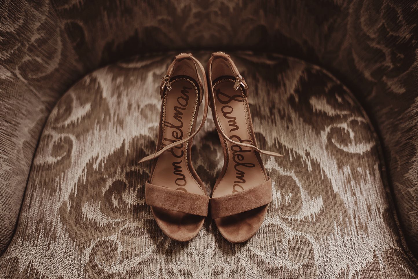 Sam Edelman tan suede heeled sandals displayed on a vintage patterned armchair for a wedding.