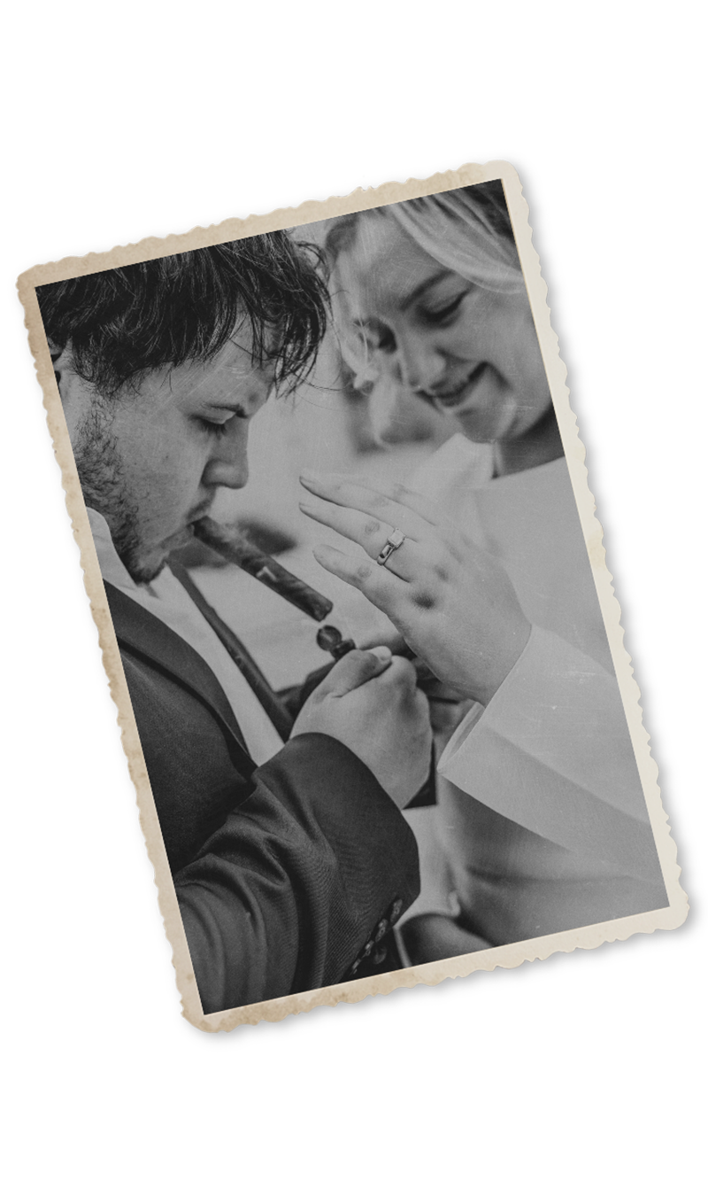 Black and white vintage-style photo of a groom kissing bride's hand, showcasing her wedding ring at a romantic ceremony.