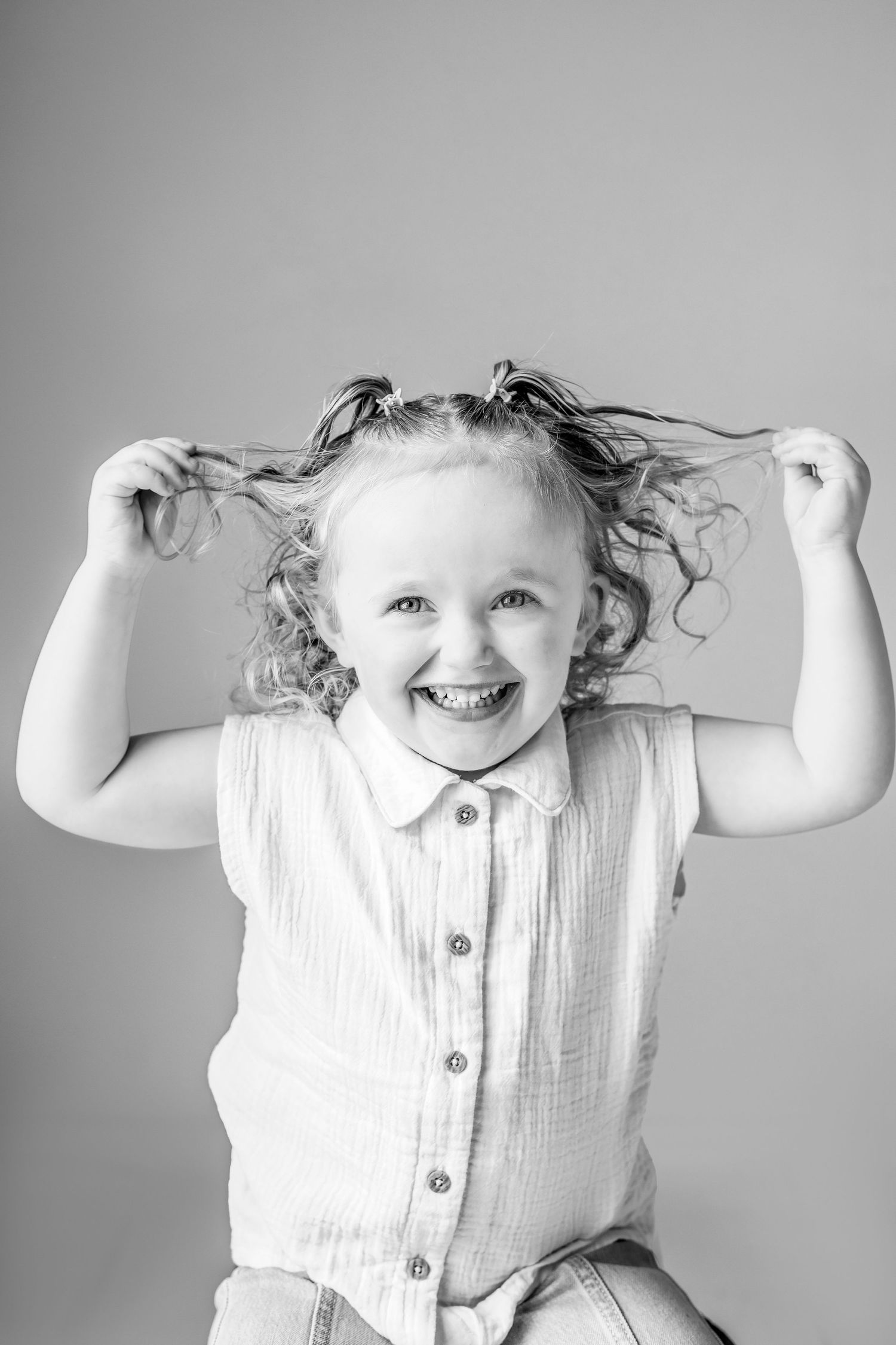 Cheerful black and white portrait with hands pulling curly pigtails in white shirt.