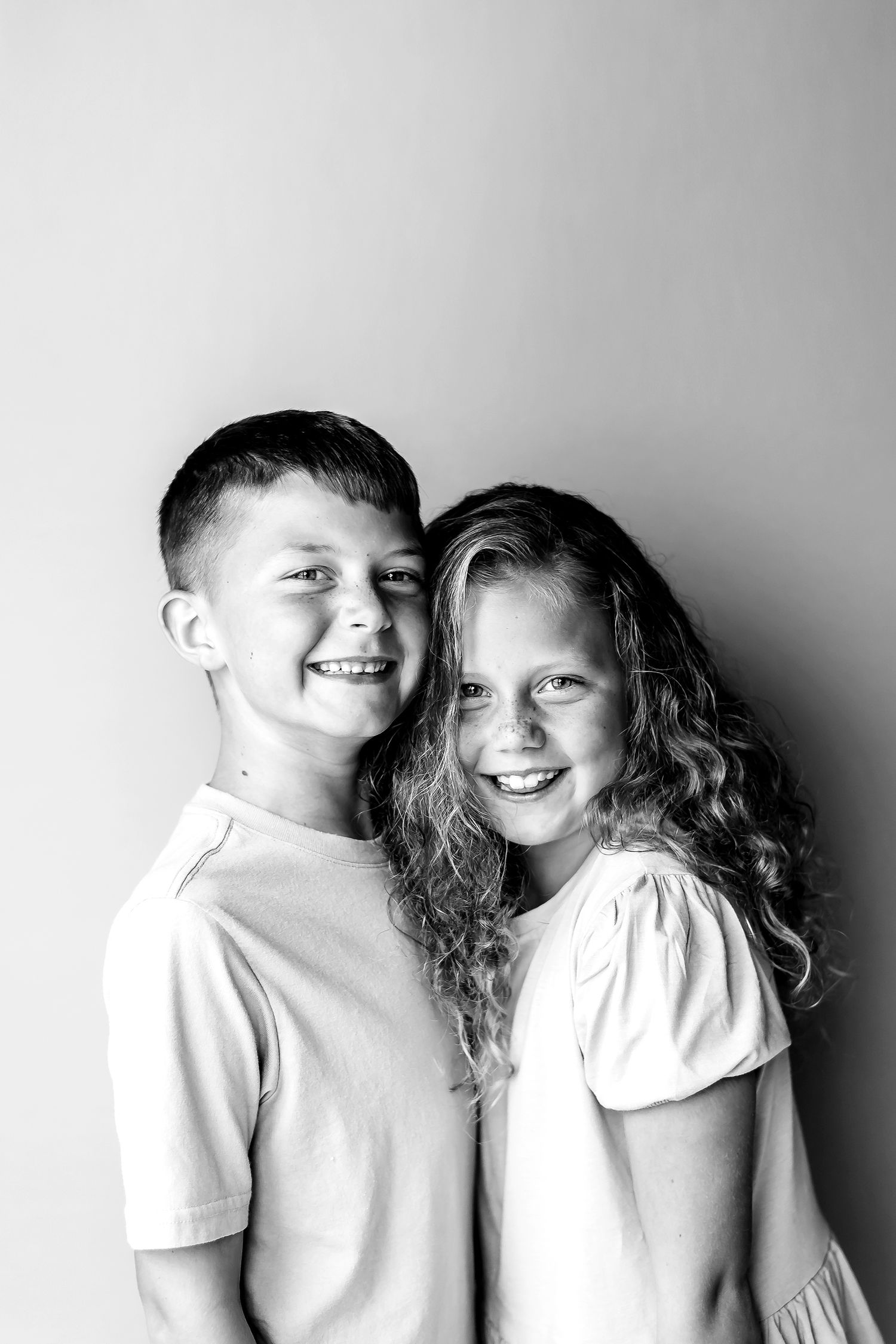 Black and white portrait of siblings smiling together against a plain background.