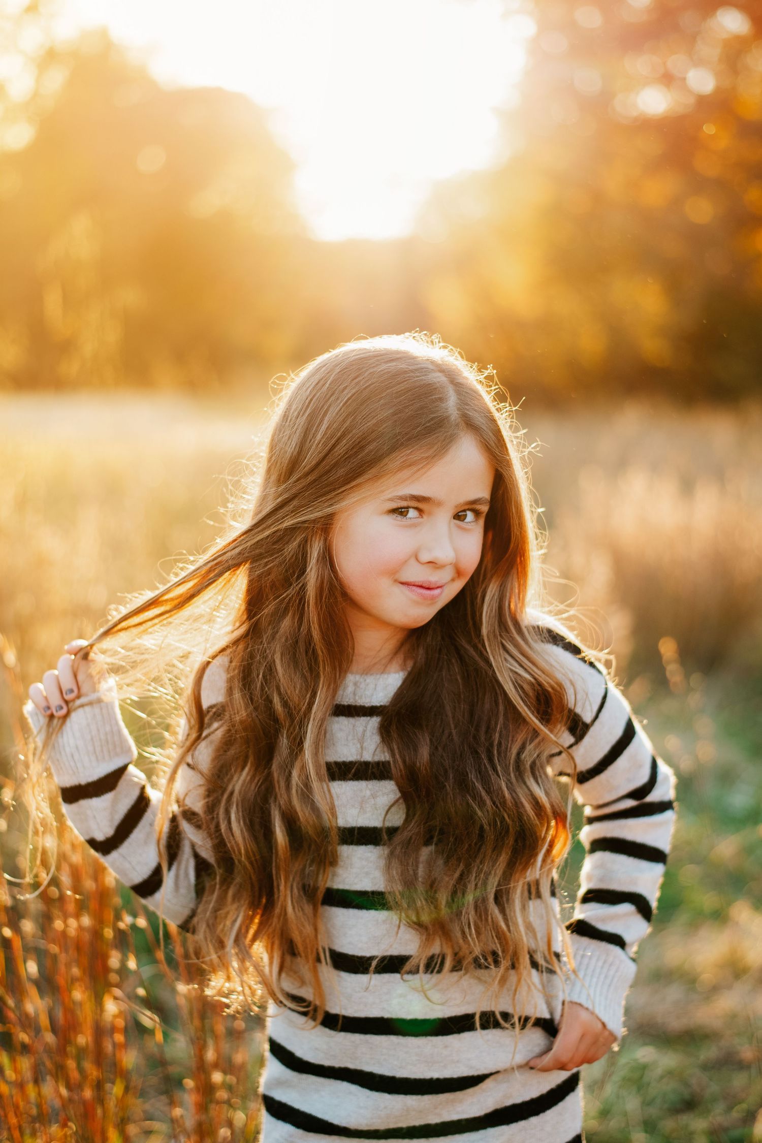 Portrait with flowing hair wearing striped sweater in golden hour lighting.
