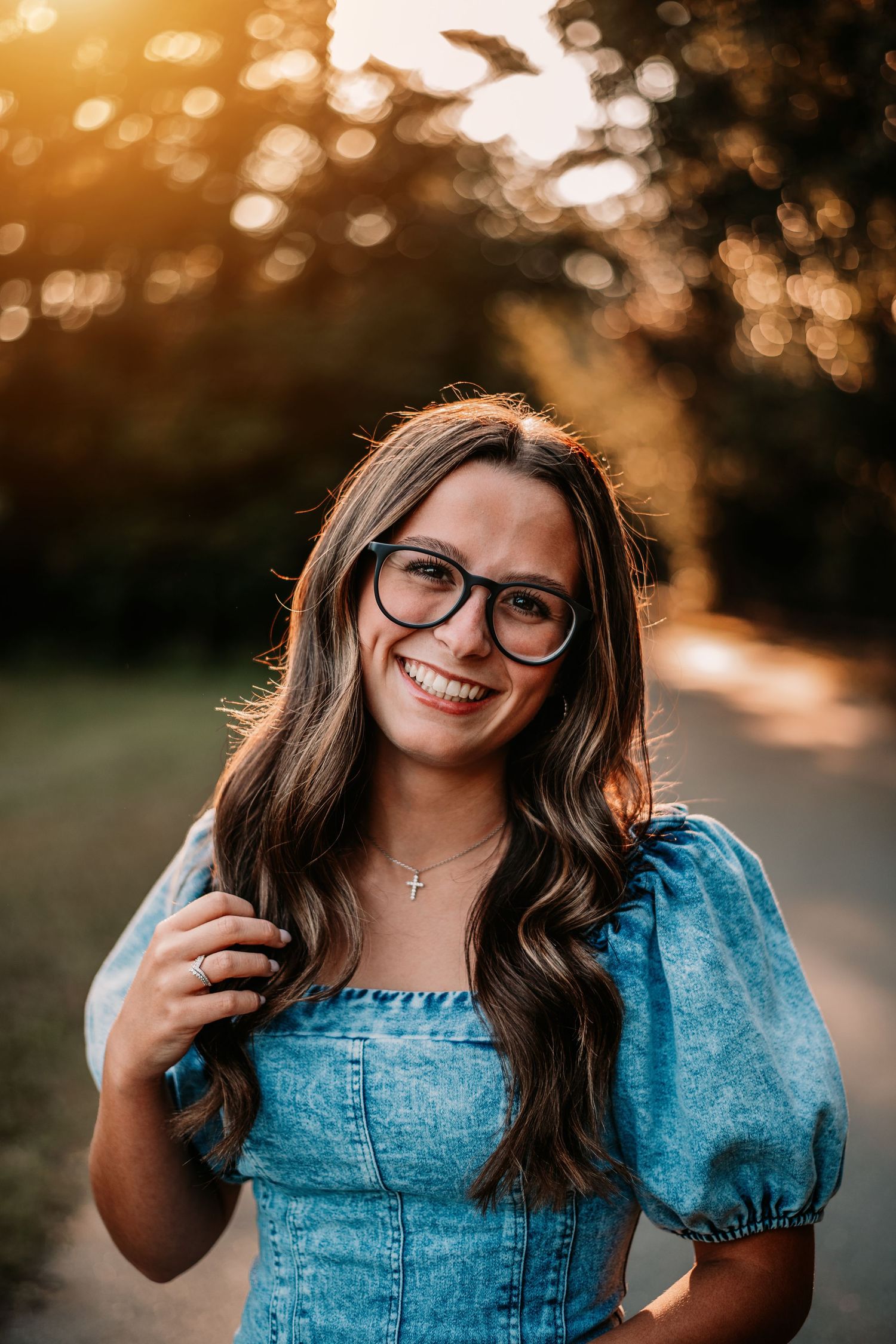 Portrait of woman in blue denim dress and glasses during sunset.