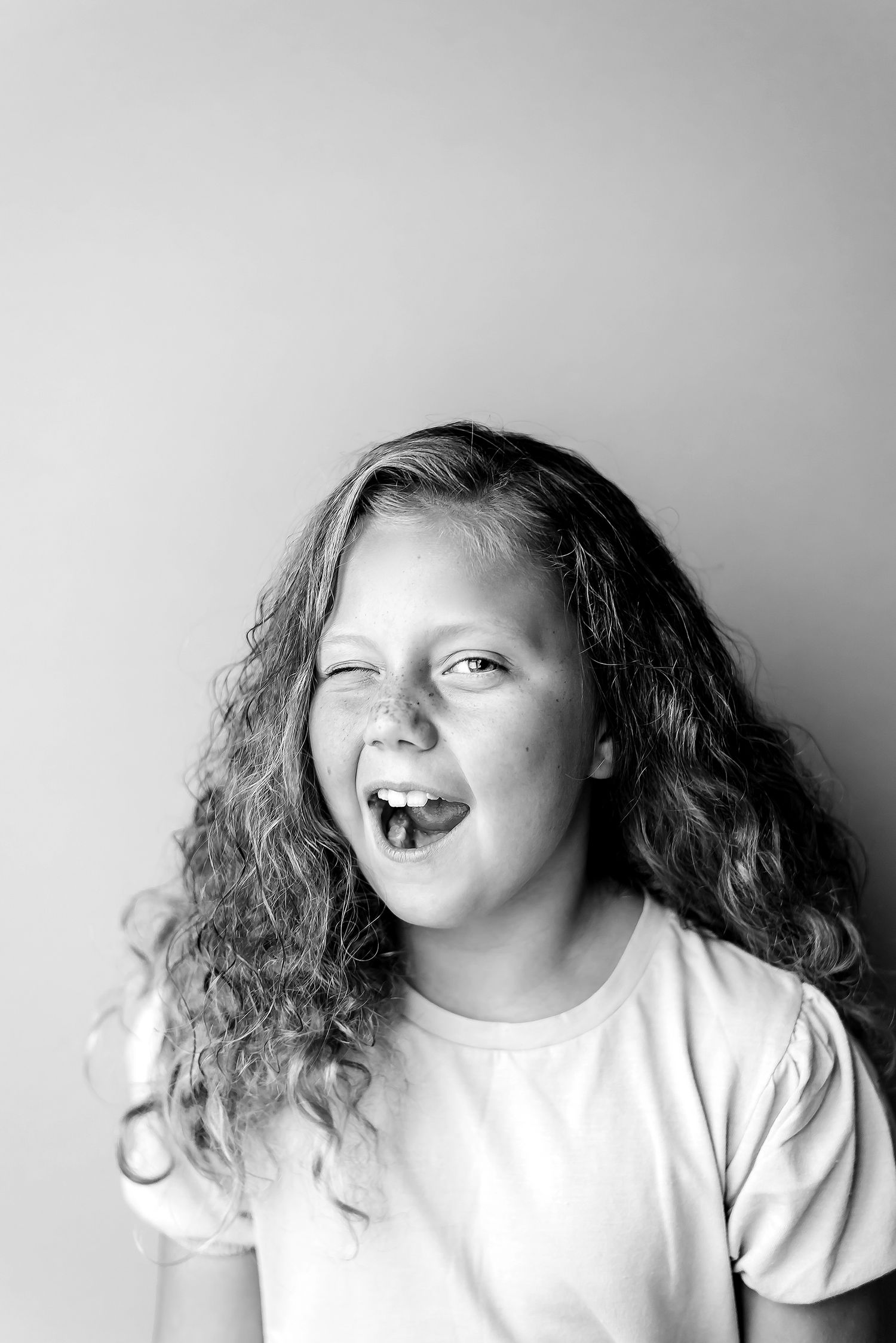 A series of black and white portraits showing someone with curly hair in a white shirt making playful expressions.