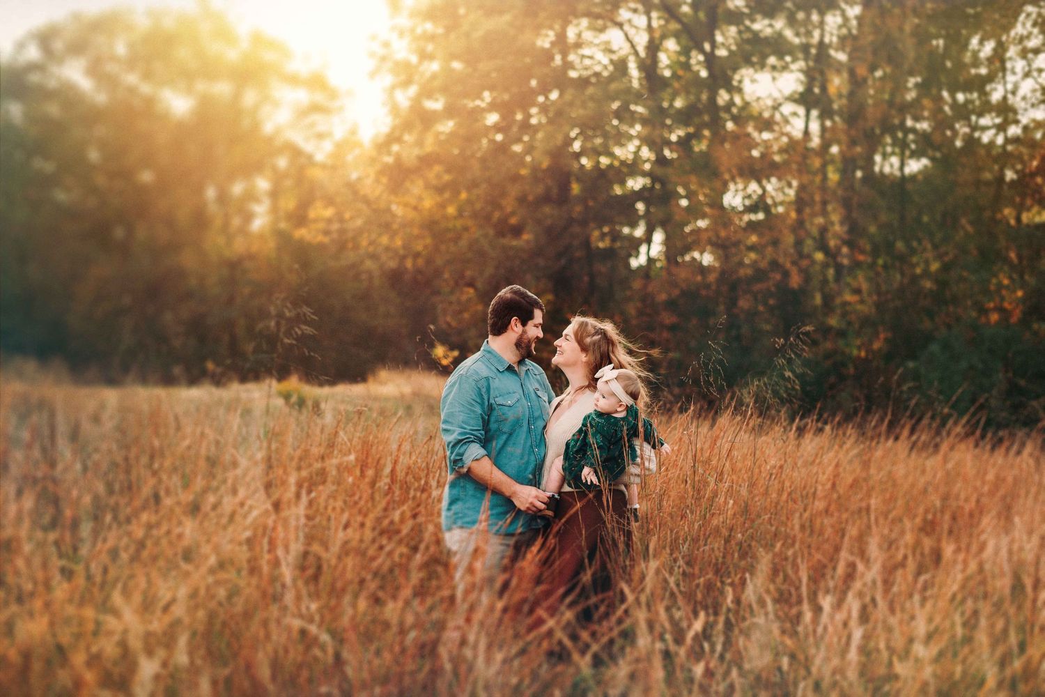 Romantic sunset photoshoot in a golden field with warm evening light filtering through trees.