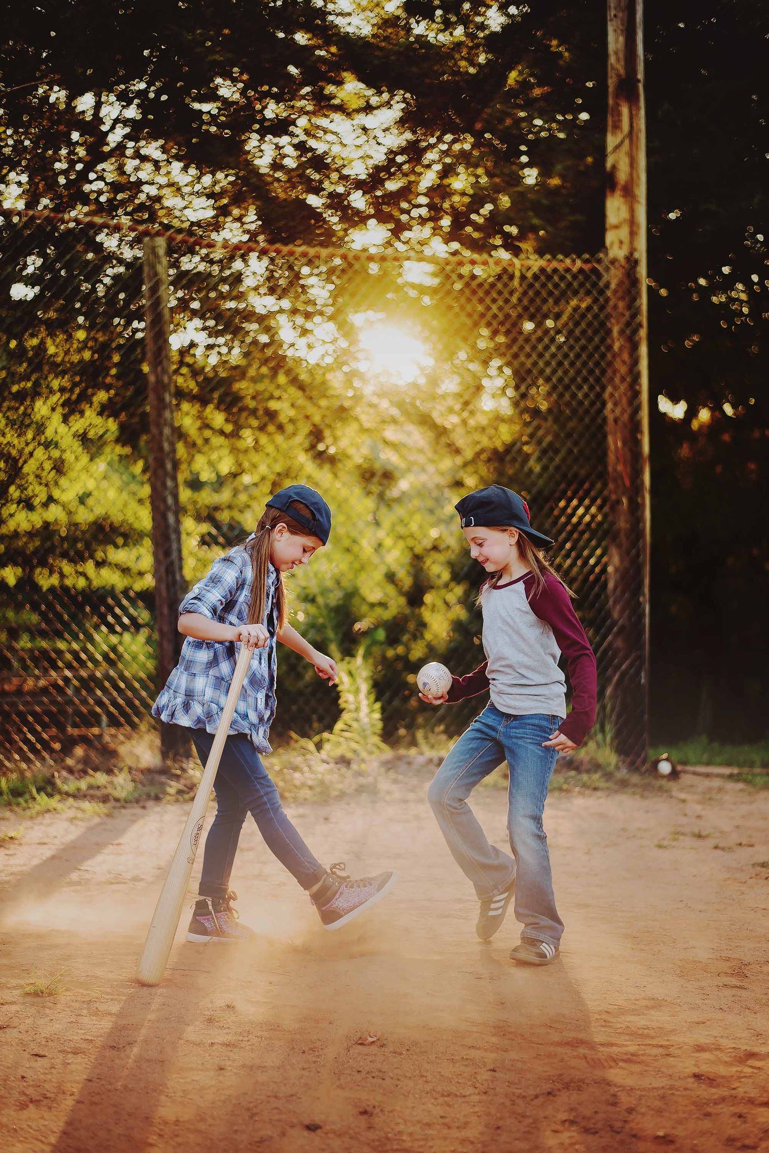 Two children play baseball on a dusty field at sunset with golden sunlight streaming through the trees.