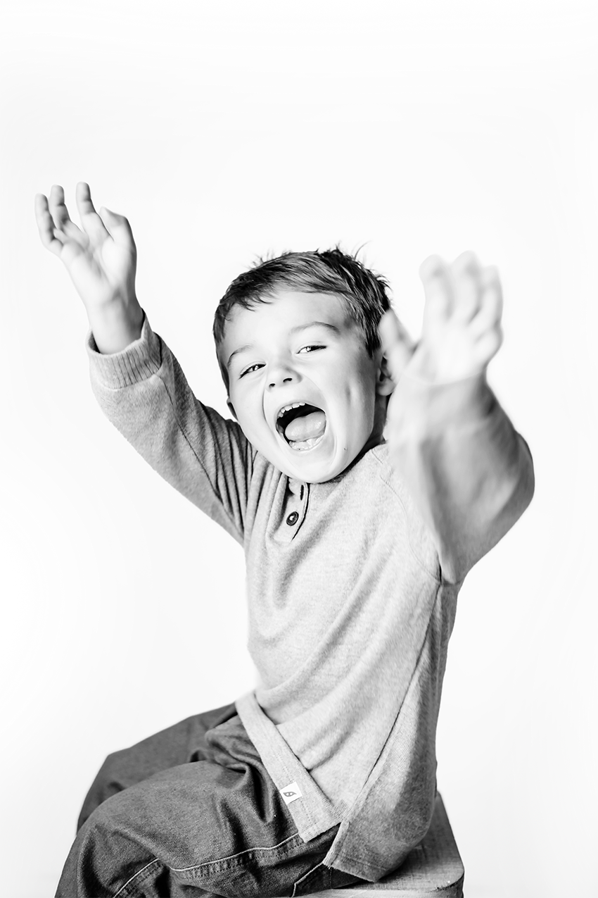 A joyful child in a light gray sweatshirt jumps and plays energetically against a white background.