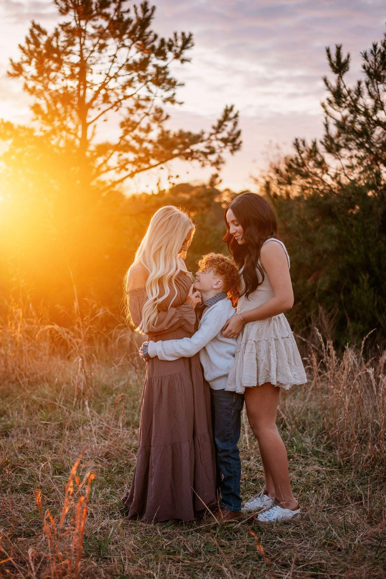 Family embraces in golden sunlit field during sunset portrait session.