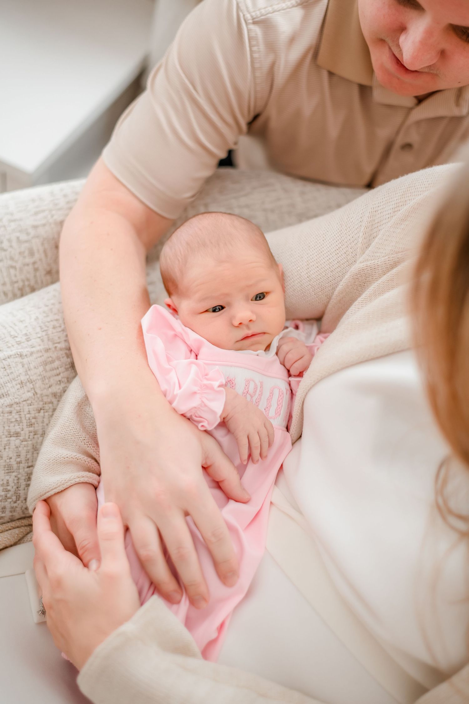 A newborn baby in pink clothing rests peacefully in their parents' arms.