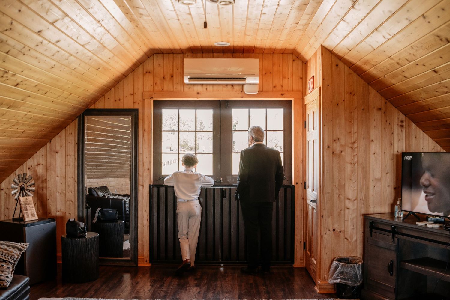 Bride and groom stand at a wooden cabin door with vaulted pine ceiling, sharing a quiet moment before their ceremony.