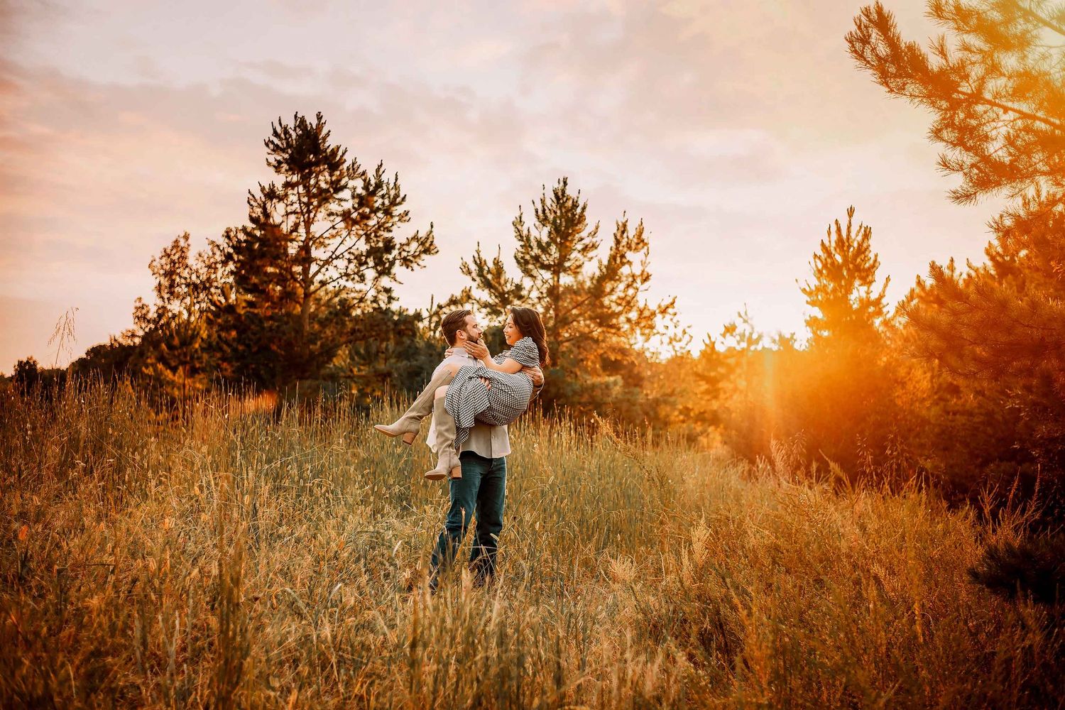 Couple embracing in golden sunset light in a meadow surrounded by autumn trees.