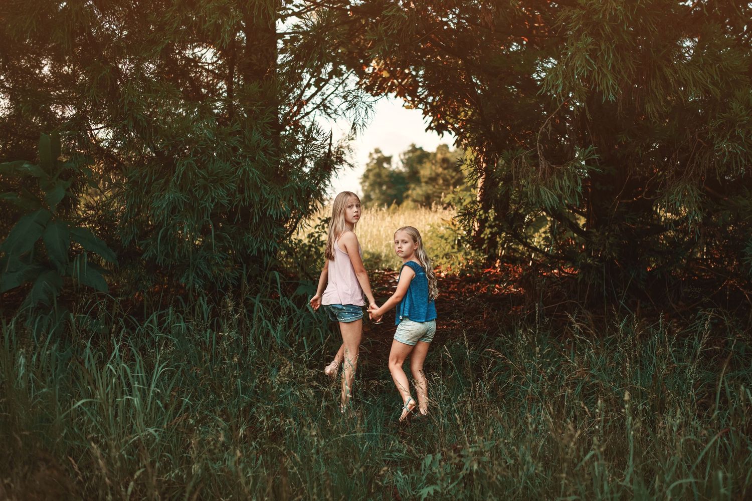 Children playing and jumping in tall grass during evening golden hour.