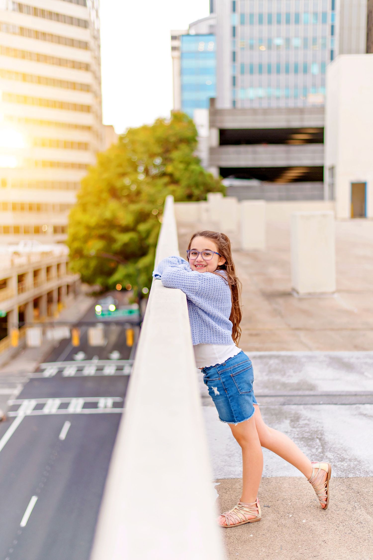 Person leaning against rooftop wall overlooking city street during sunset.
