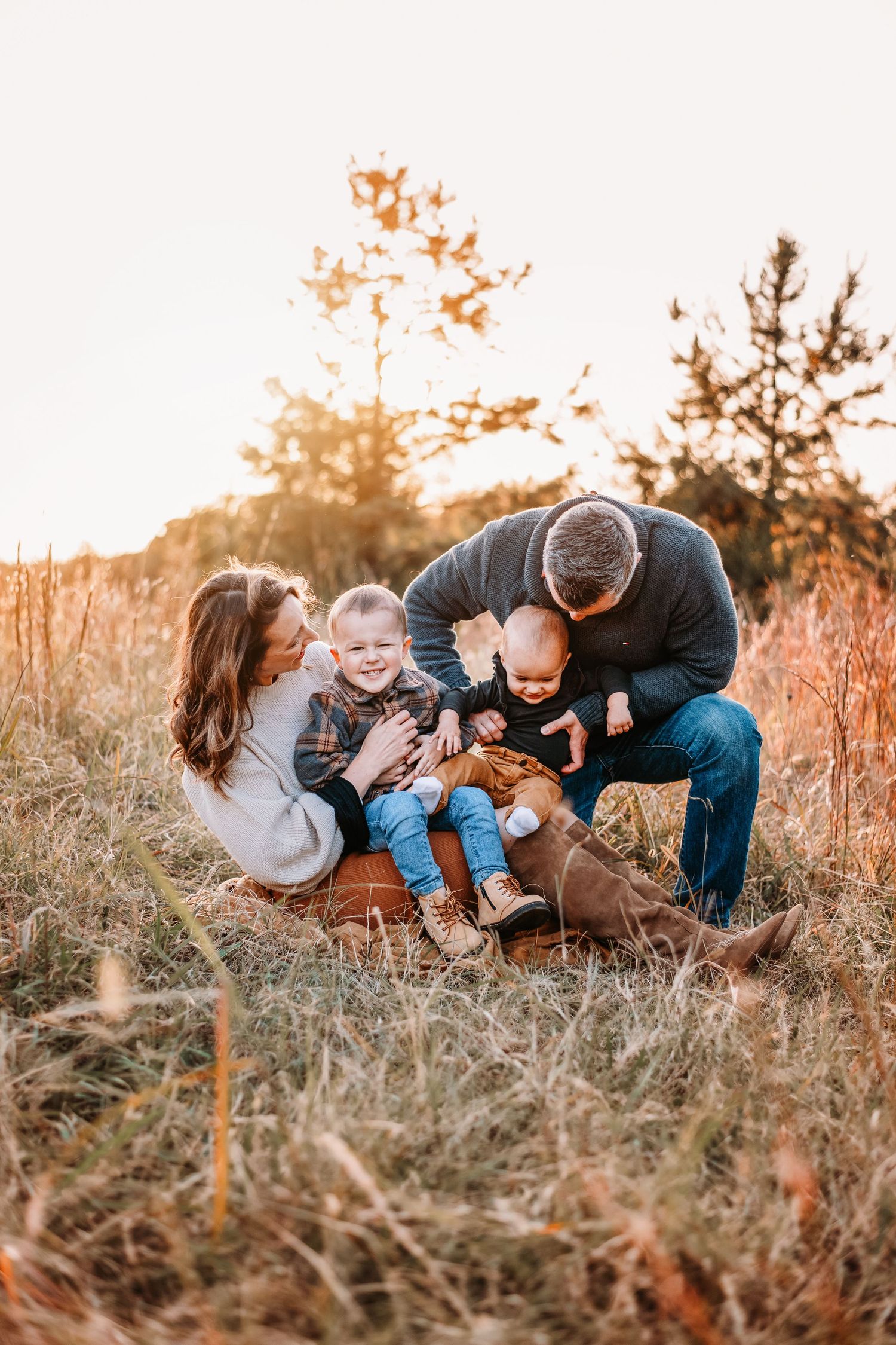 Family playfully interacting in golden field during sunset photoshoot.