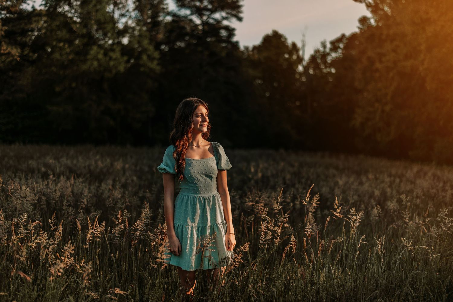 Person in teal dress standing in a golden field at sunset.