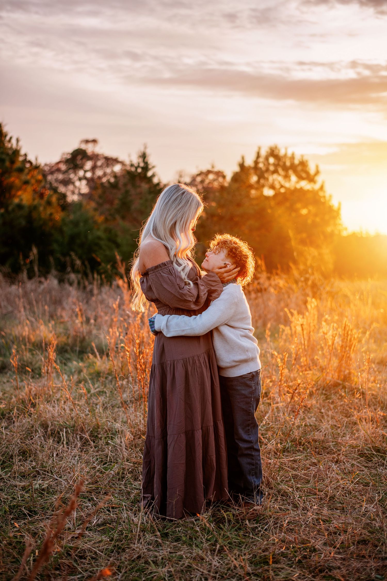 Mother and child share a tender moment in a sunlit field at sunset.