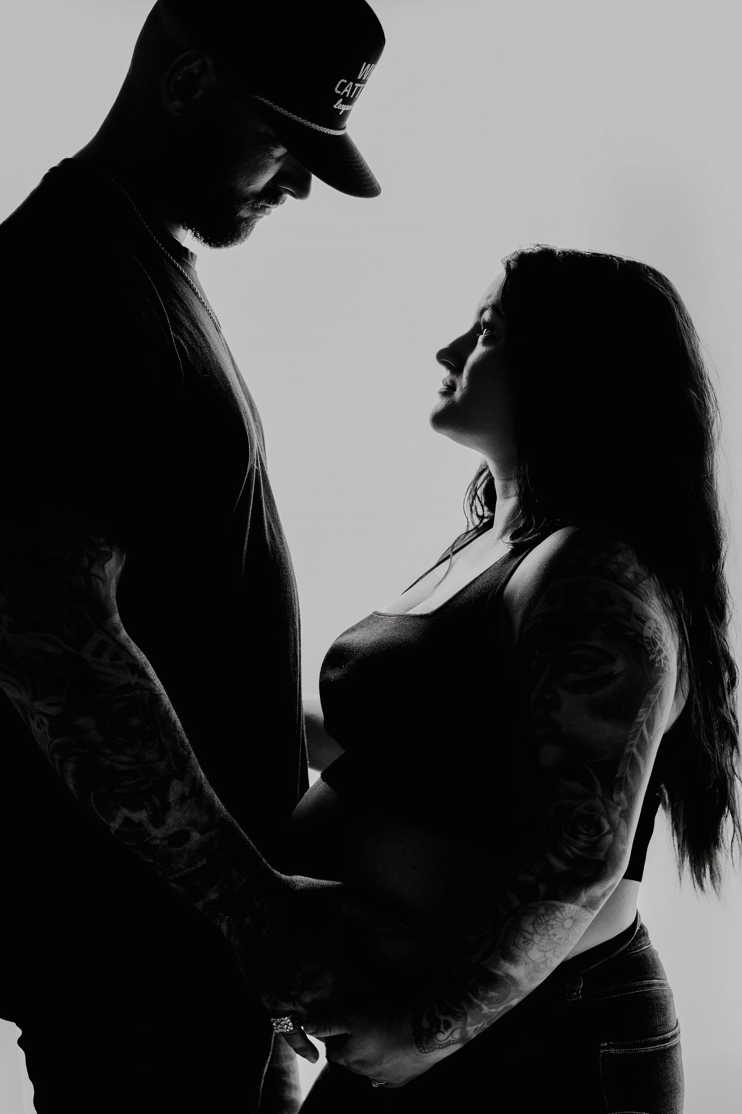 Silhouette portrait of a couple in an intimate pose against a light background.