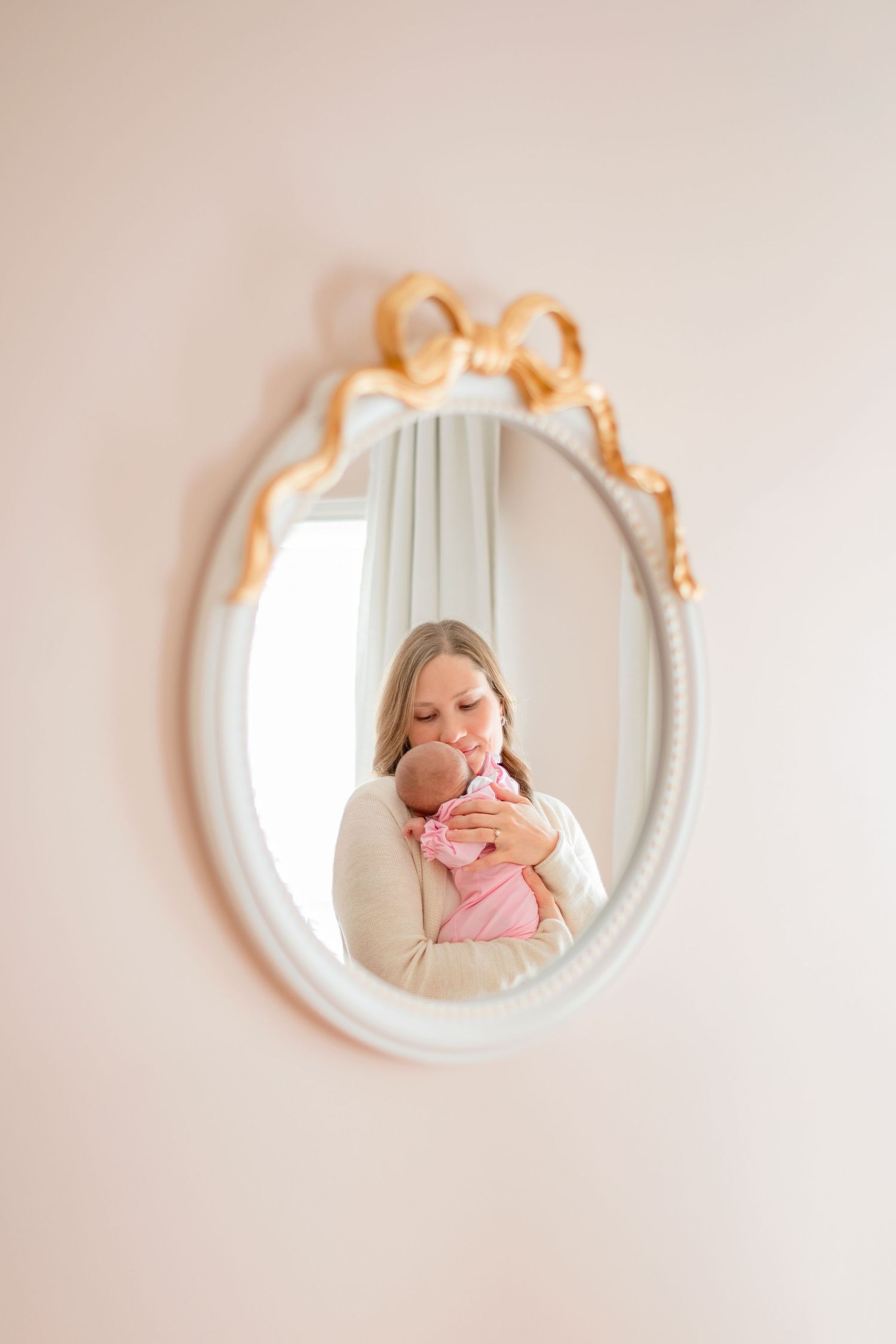 A reflection in an ornate white mirror shows a tender moment with a baby in pink.