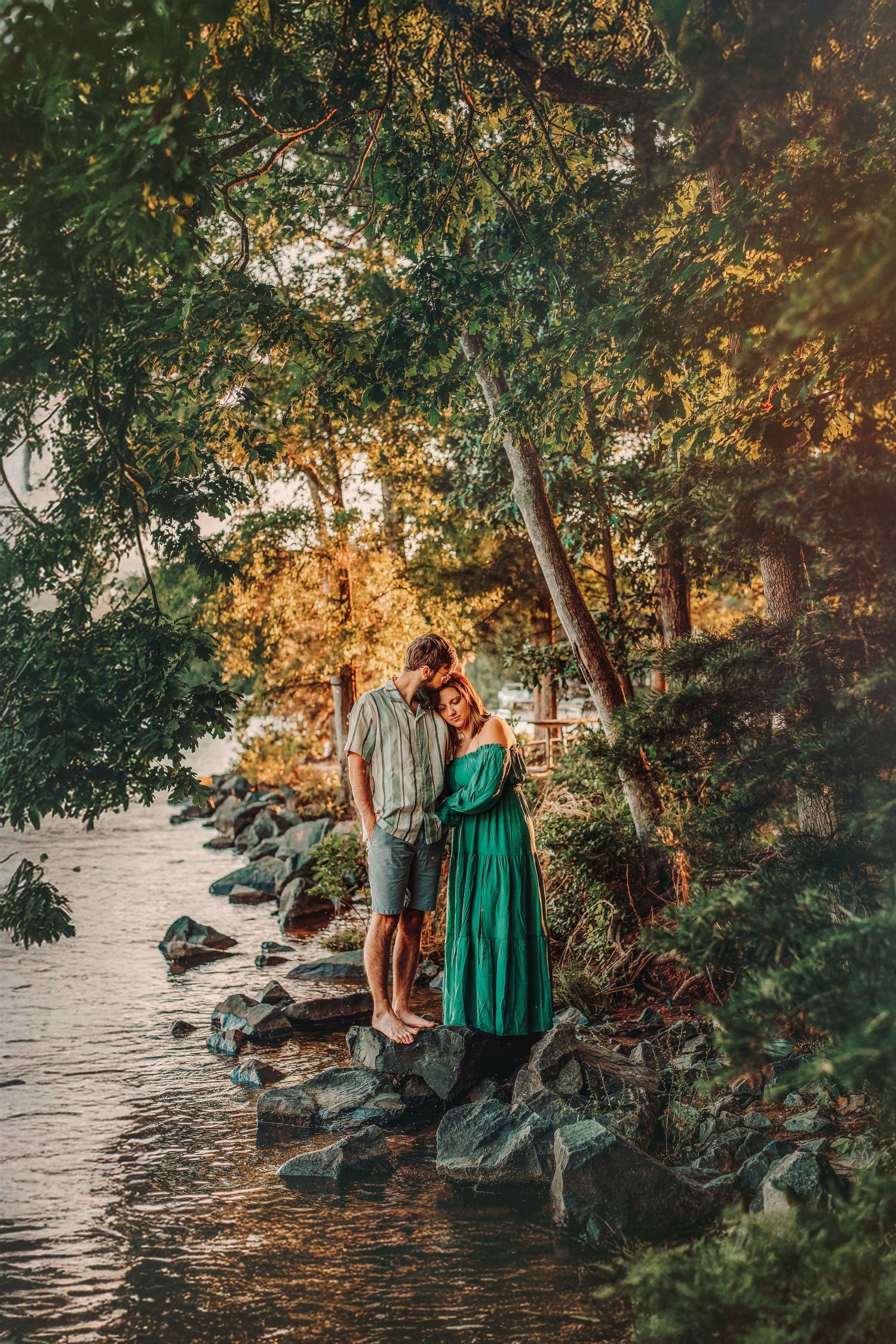 Couple enjoying a peaceful moment together by a lakeside during golden hour among trees and rocks.