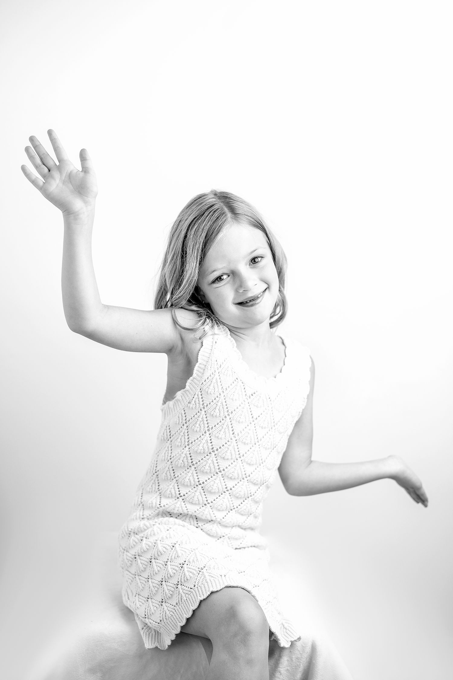 A black and white photo series showing a child in a white lace dress striking playful dance poses against a plain backdrop.