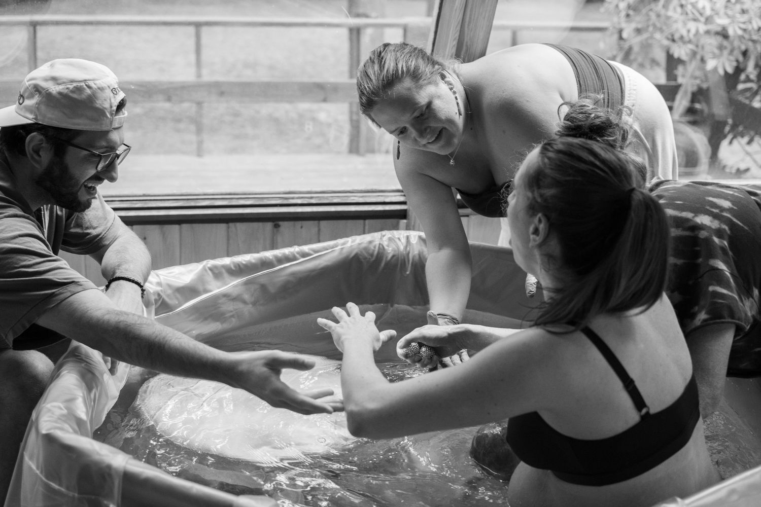 Black and white photo of a water birth with midwife and support person assisting a woman in a birthing pool.