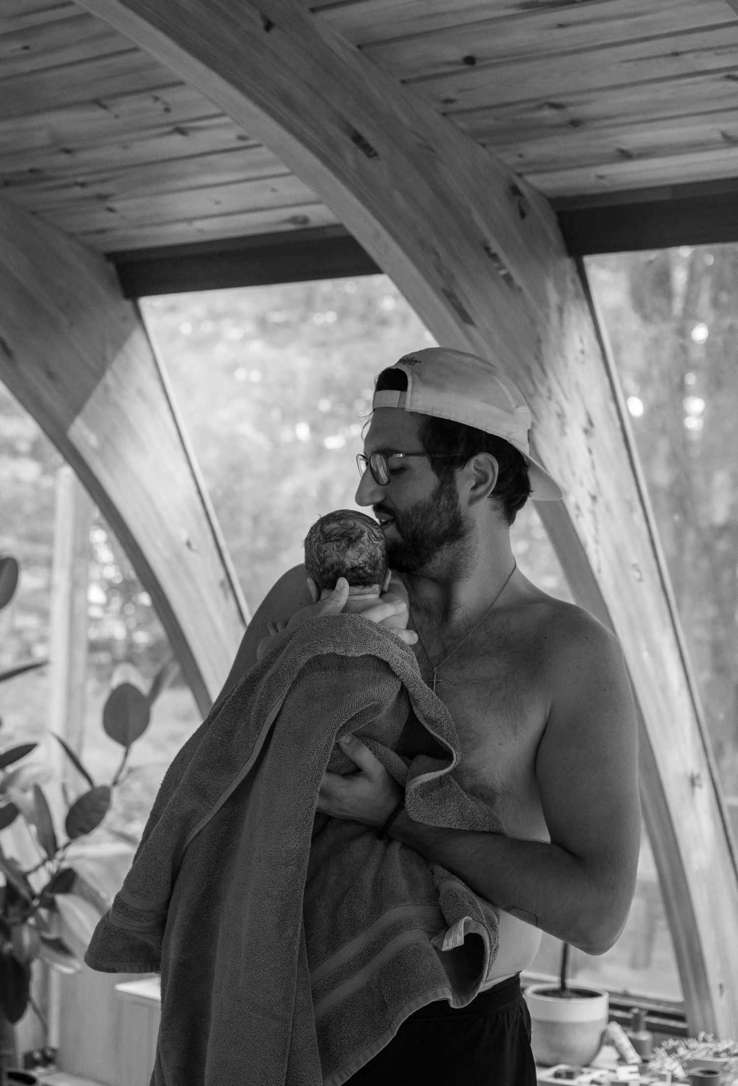 Dad performing skin to skin for his a newborn baby wrapped in a black and white photo.
