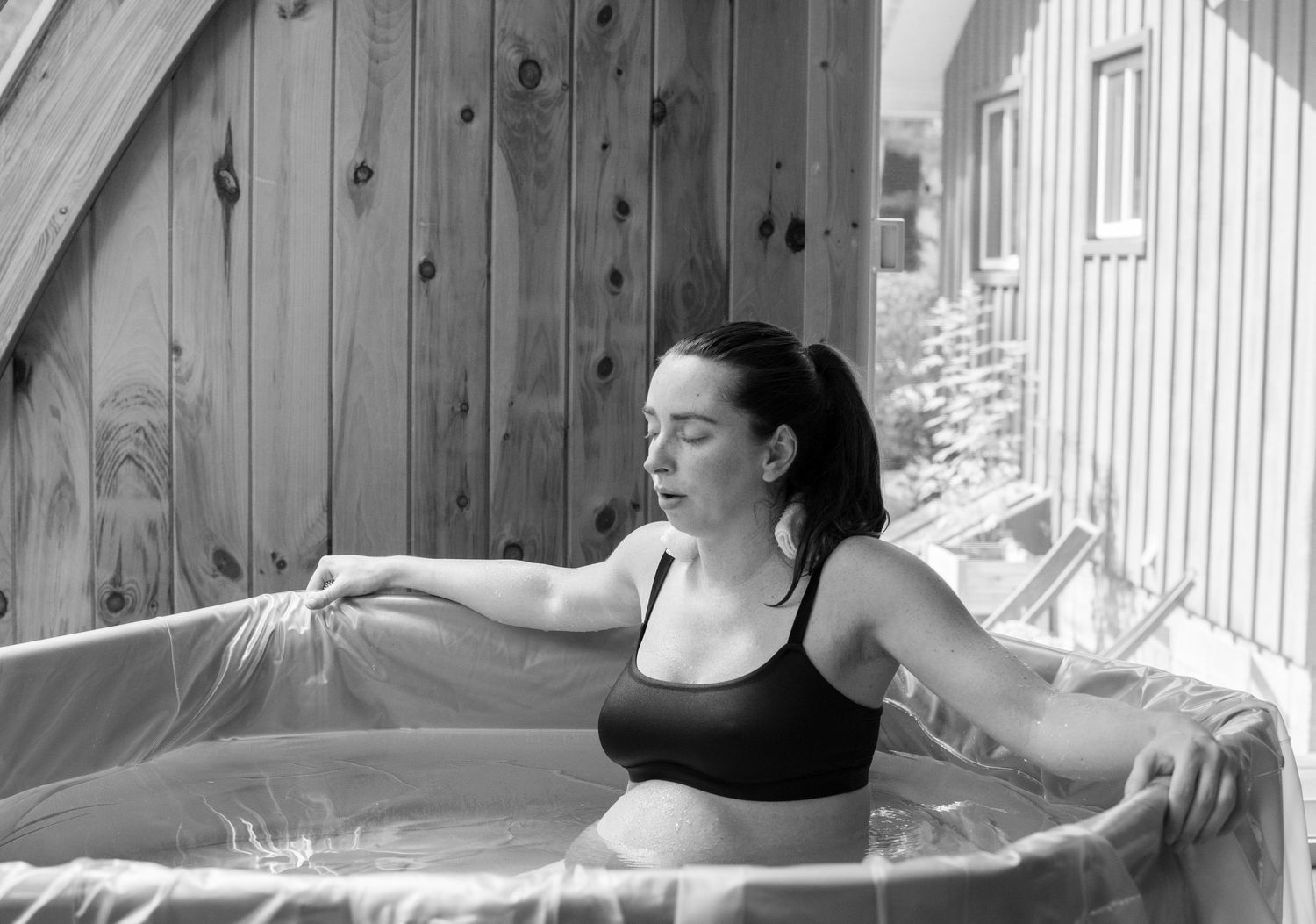 Pregnant woman relaxing in a birthing pool, black and white photo in a wooden indoor space.