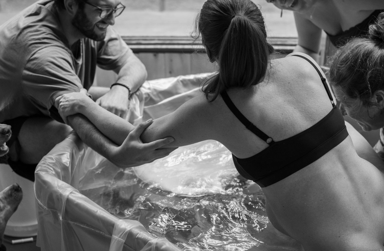 Black and white photo of a water birth, with a woman in a birthing pool assisted by medical professionals.