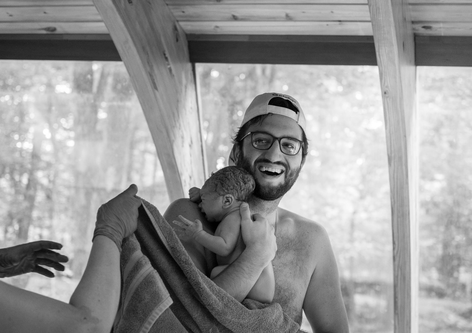 Dad performing skin to skin for his a newborn baby wrapped in a black and white photo.