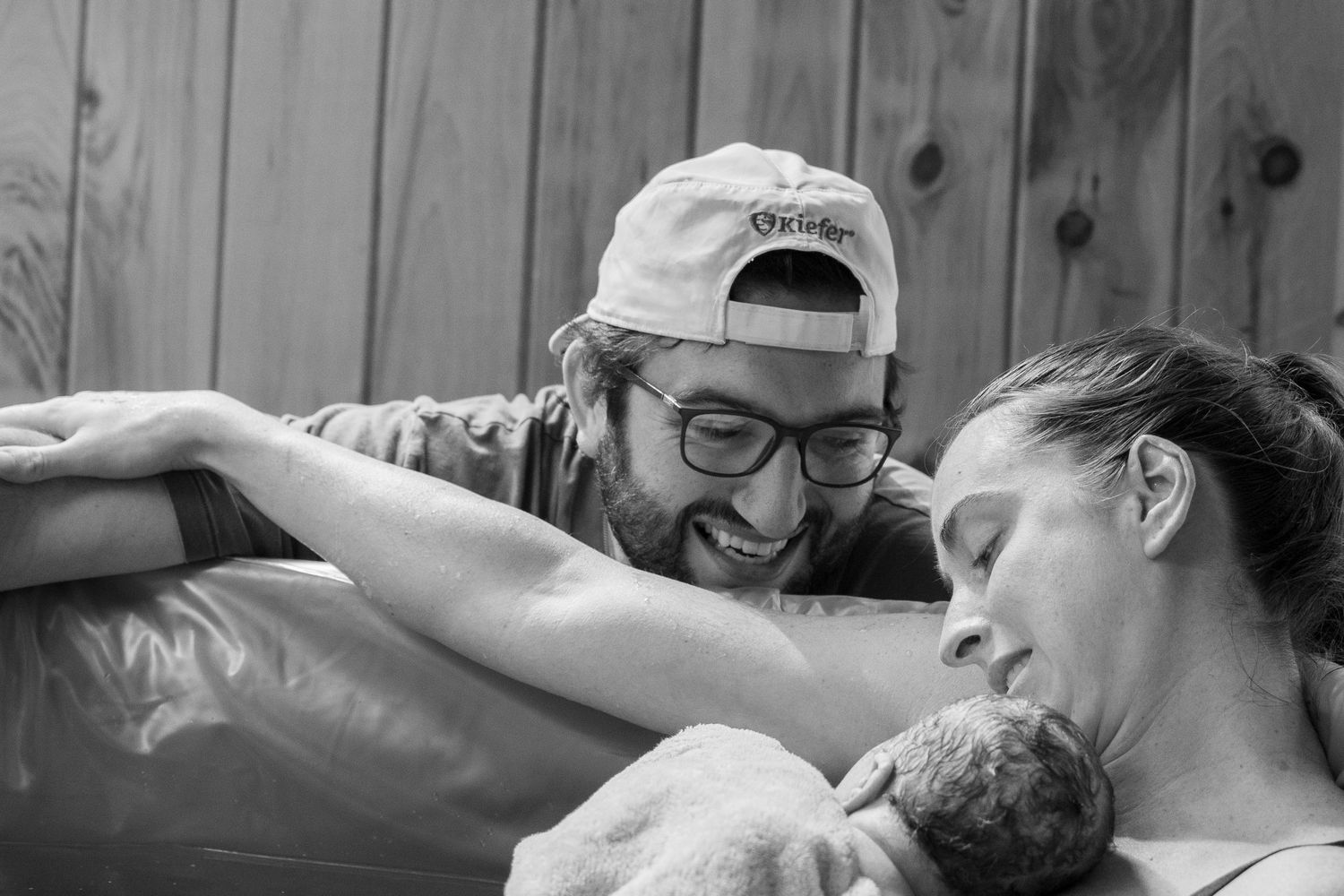 Black and white photo of parents smiling at their newborn baby during a water birth.