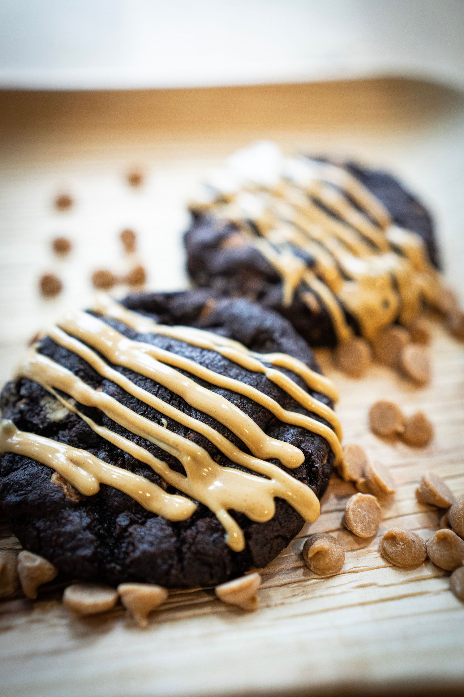Two chocolate cookies drizzled with caramel sauce sit on a rustic wooden surface, embodying the artistry of Wicked Whisk Bakery.