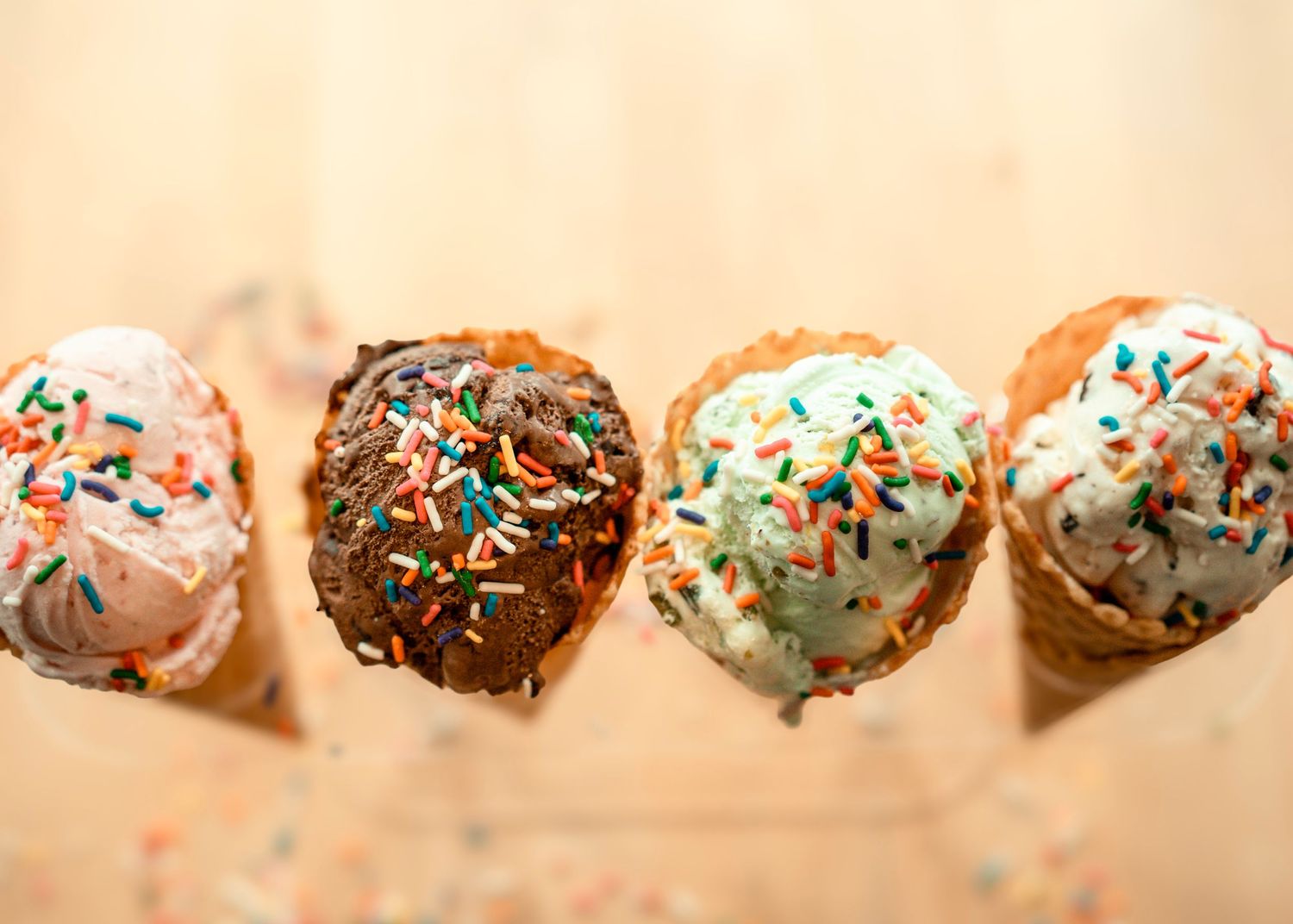 Downward facing photo of four ice-cream cones in various flavors. strawberry, chocolate, mint-chocolate chip and vanilla covered in sprinkle