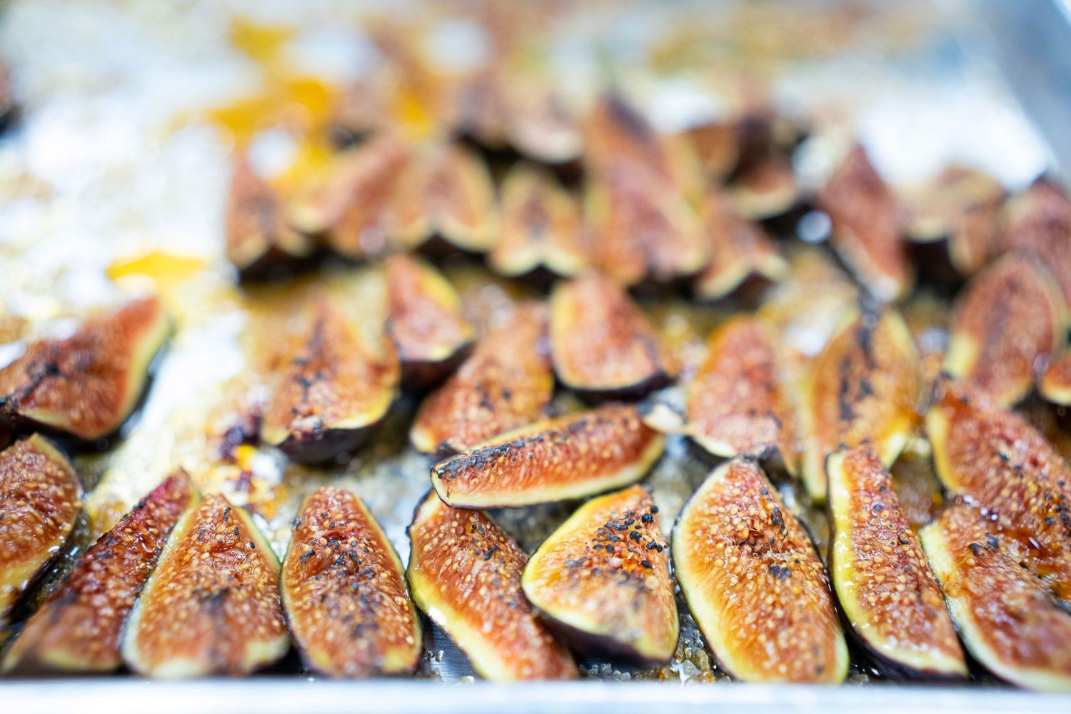 Close-up of roasted figs on a baking tray, golden-brown with caramelized edges. The figs are sliced in halves and arranged randomly.