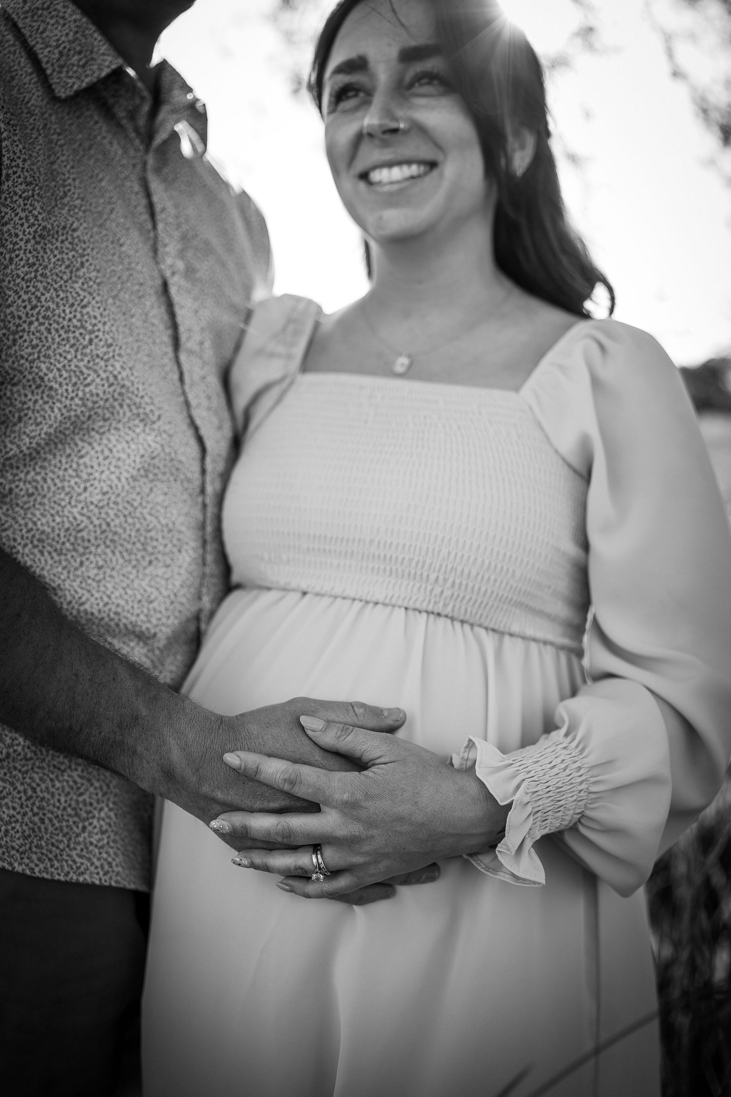 A pregnant woman holding her stomach. Man is also holding her stomach. She has light blue nails and light pink flowy dress.