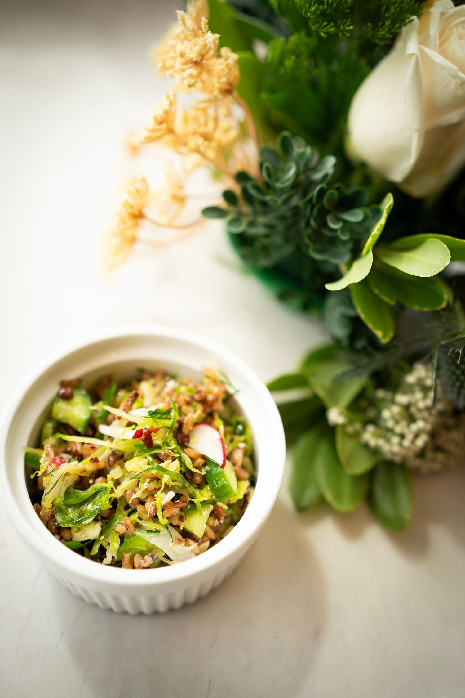 A small bowl of salad, artfully prepared by a private chef, features sliced radishes, greens, and an array of finely chopped vegetables.
