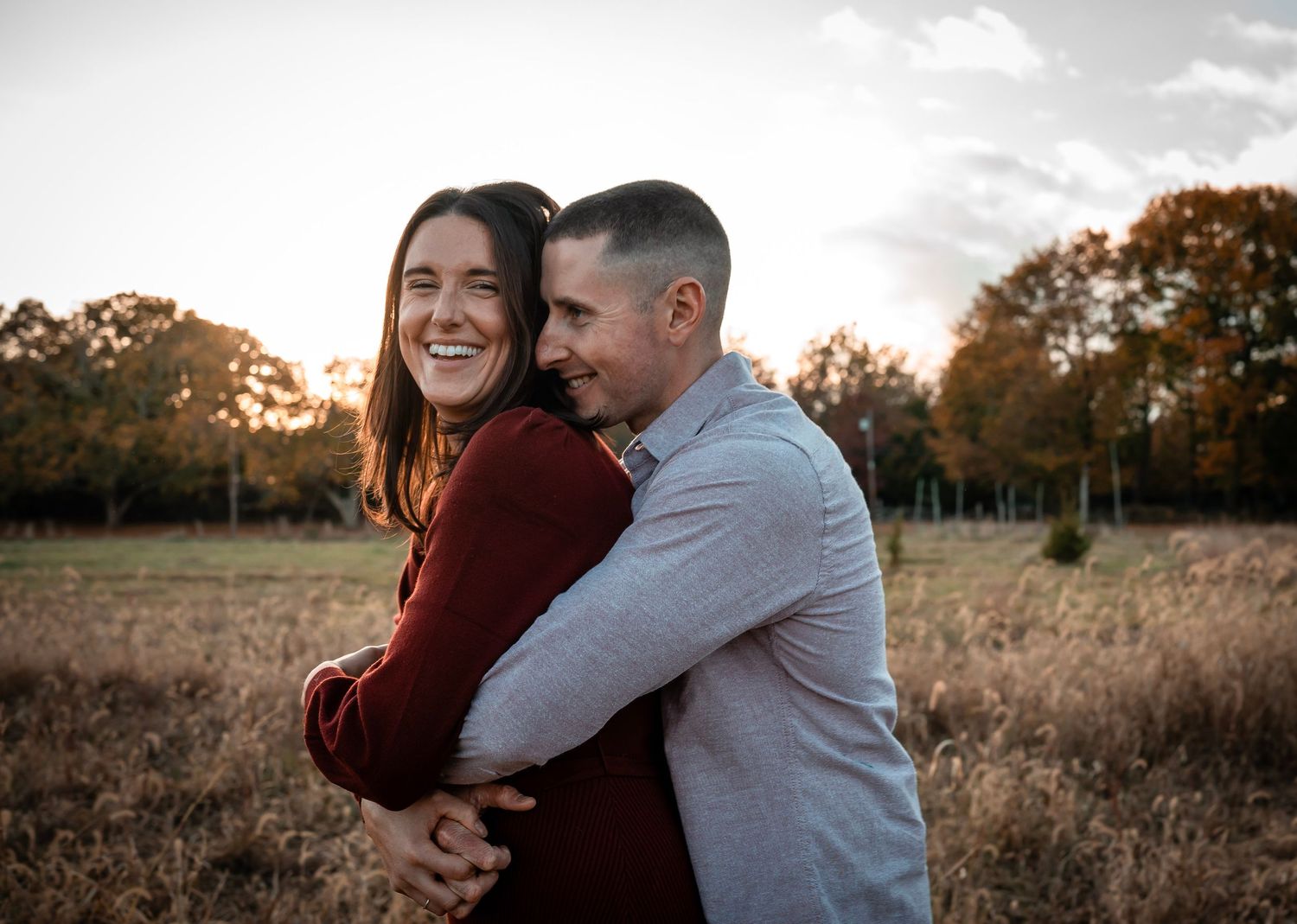 A couple embracing each other in a  field during golden hour. The couple dressed in formal attire stands close and are in love.