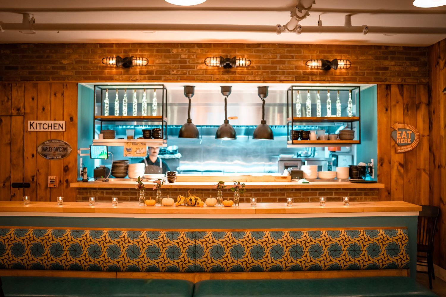 Cozy restaurant kitchen with a blue and gold patterned counter, and wooden walls. The kitchen area is visible through a large window.