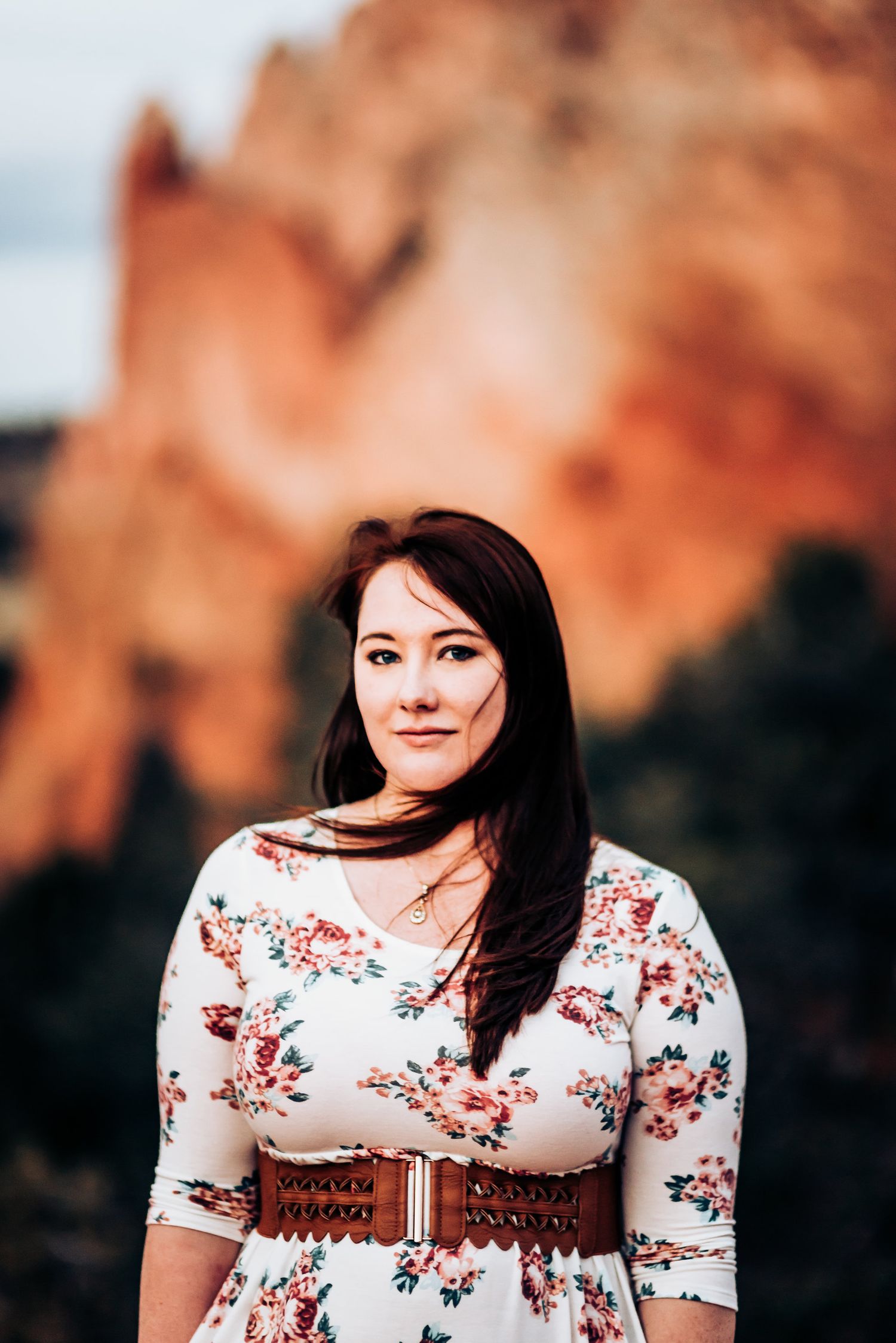 Portrait of woman in floral dress against dramatic red rock formation backdrop.